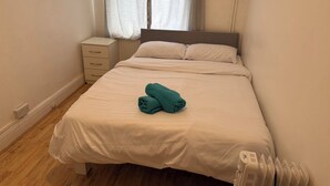 A neatly made bed with a folded towel, a bedside table, and a radiator. - Rahal Hotel Hackney London (London)