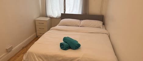 A neatly made bed with a folded towel, a bedside table, and a radiator.