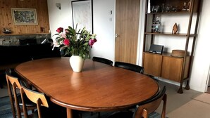 A wooden dining table with six chairs, a vase of flowers, and a kitchen area in the background. - Midcentury 3-bed House in Gairloch (Gairloch)
