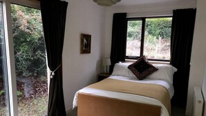 A bedroom with a large bed, a nightstand, a lamp, and a window with curtains. - Midcentury 3-bed House in Gairloch (Gairloch)