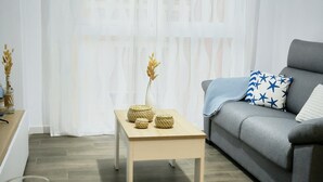 Uma sala de estar moderna com um sofá cinza, uma mesa de centro de madeira e uma área de jantar com uma tigela e pratos.