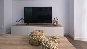 Uma sala de estar moderna com uma TV de tela plana em um armário branco, pufes de vime e figuras decorativas de peixes.