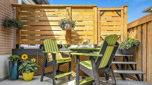 Un patio exterior con dos sillas verdes, una mesa y una valla de madera.