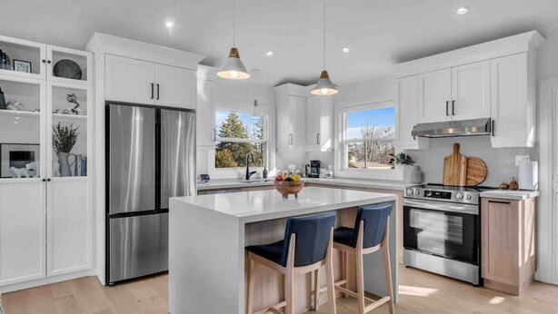 Una cocina moderna con armarios blancos, electrodomésticos de acero inoxidable y una isla central con taburetes de bar.