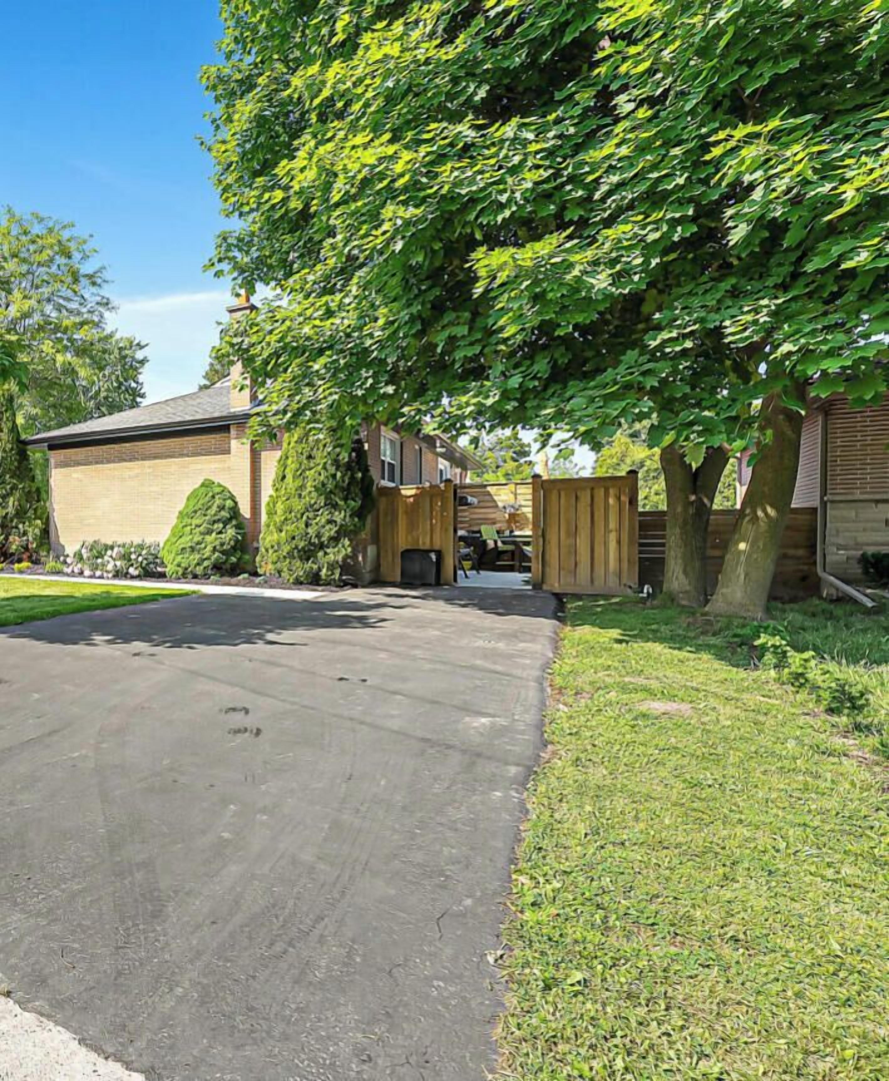 A residential driveway leading to a house with a garage, surrounded by a wooden fence and lush greenery.