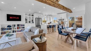 Una cocina moderna con armarios blancos, una isla central y una zona de comedor con una mesa y sillas de madera.