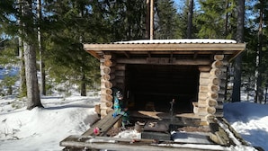 Una cabaña de troncos con techo de metal, rodeada de nieve y árboles.