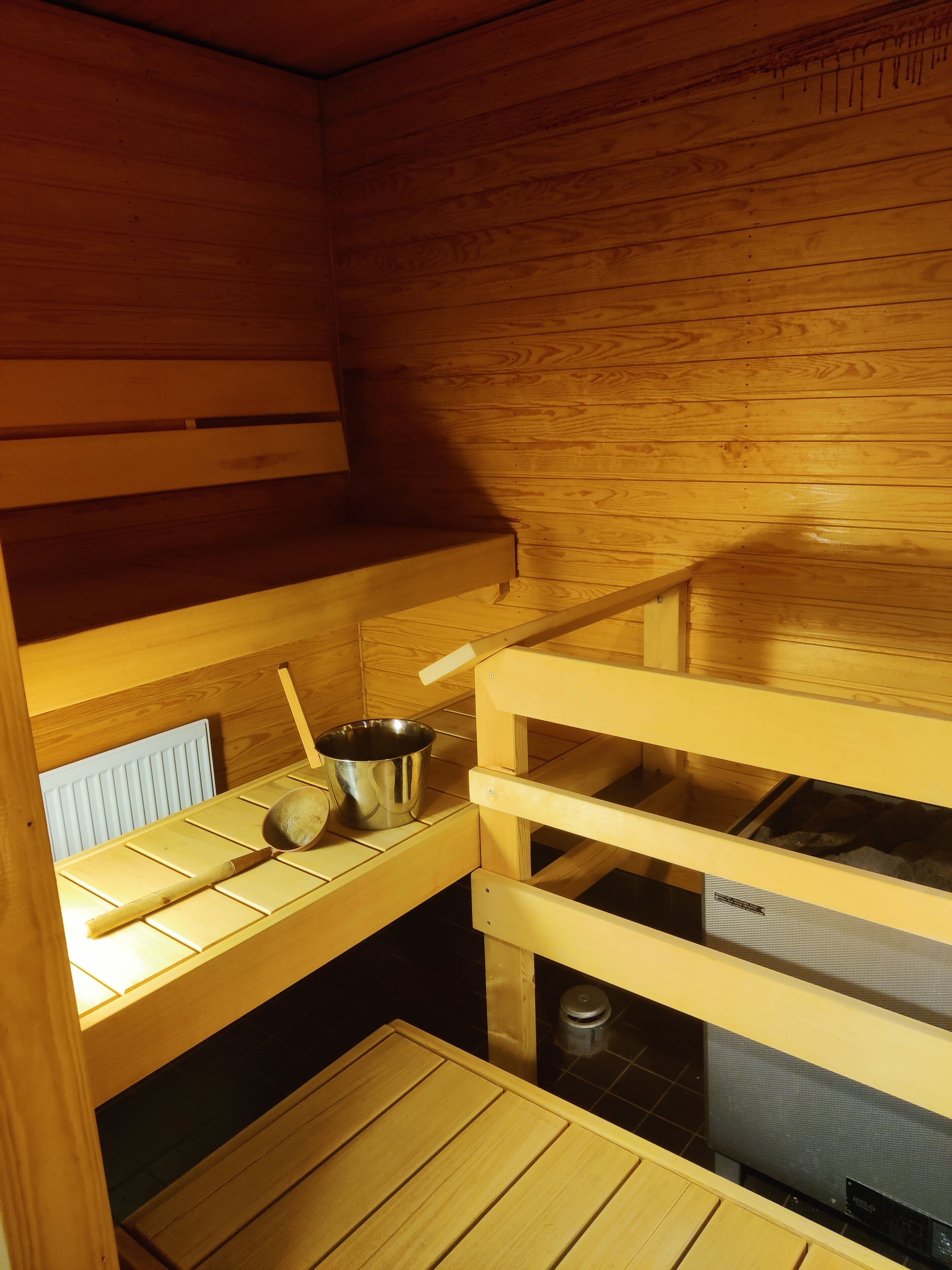 Una sala de sauna con bancos de madera, un cubo de metal y una cuchara de madera.