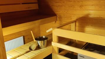 Una sala de sauna con bancos de madera, un cubo de metal y una cuchara de madera.