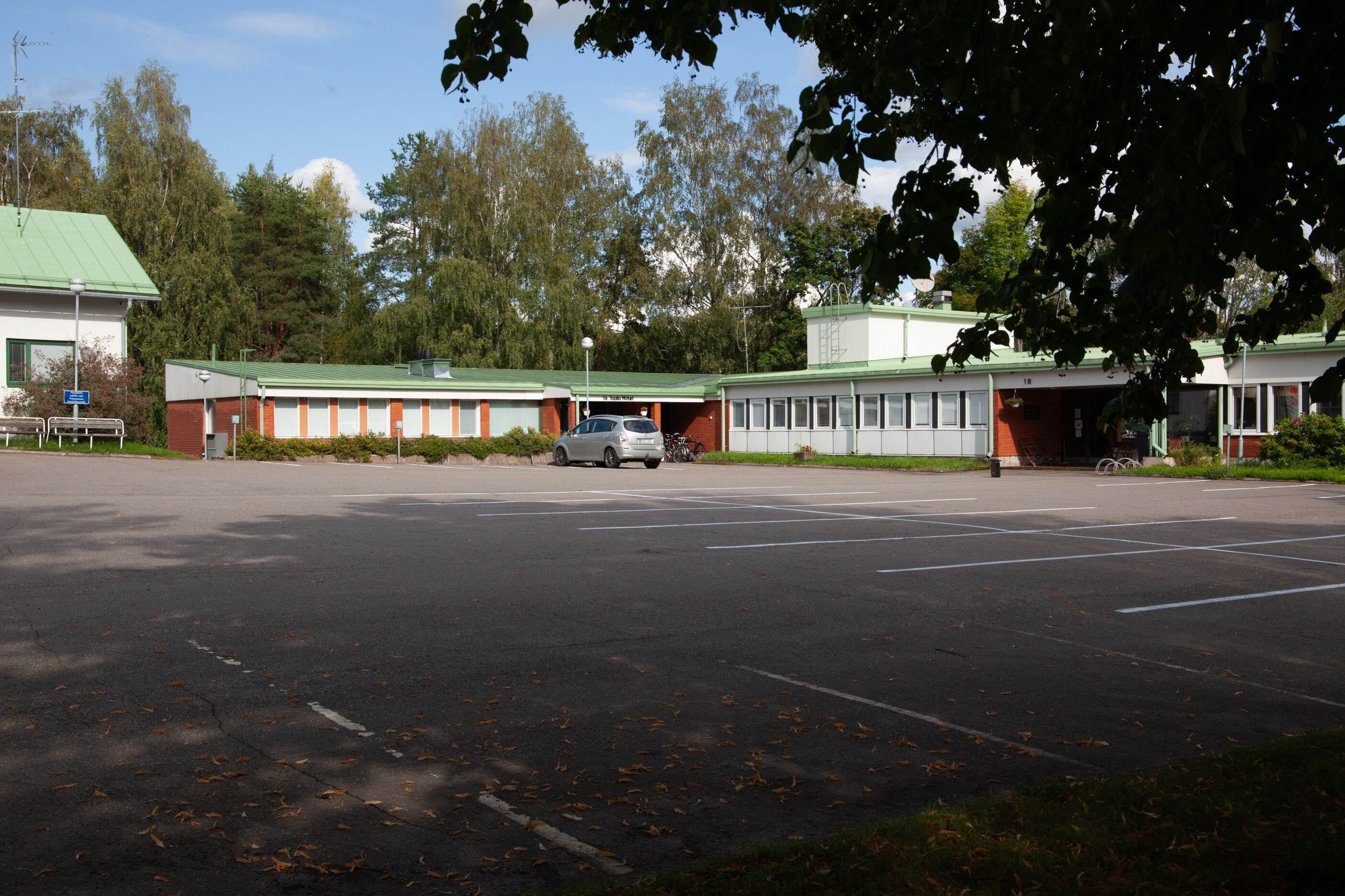 A parking lot with a building that has a green roof and a sign indicating a business or office.