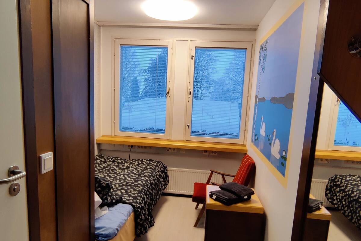 A compact room with two beds, a desk, and a window with blinds.
