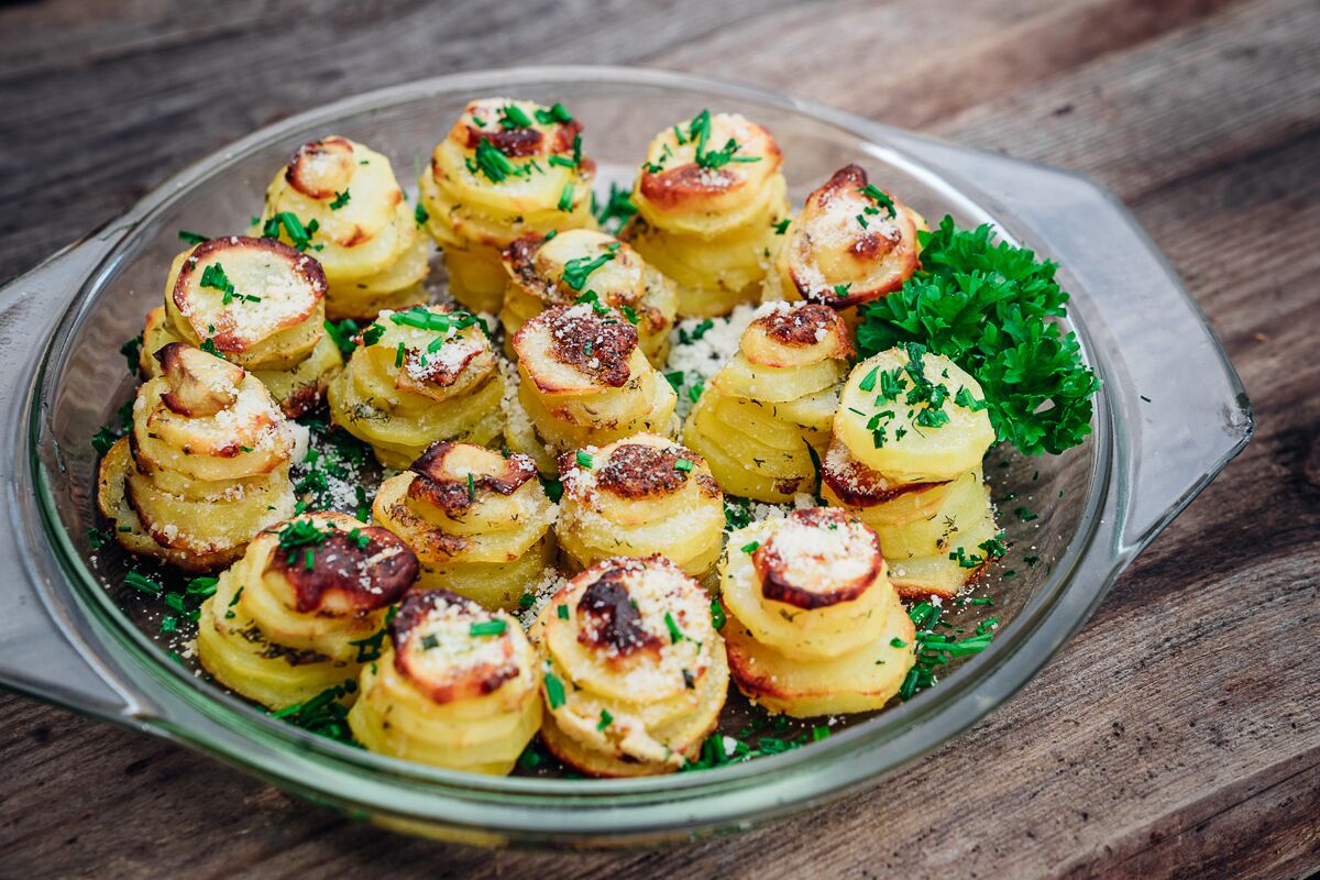 A glass dish with roasted potatoes garnished with herbs and cheese.