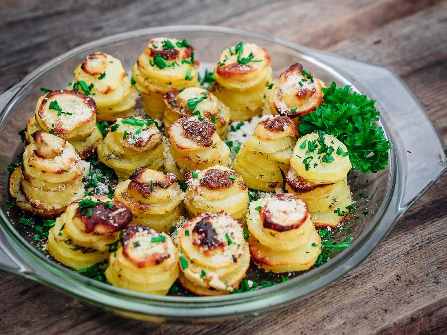 A glass dish with roasted potatoes garnished with herbs and cheese.
