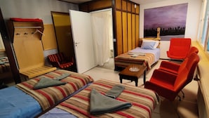 Una habitación de hotel con dos camas, un sillón rojo, una mesita y un armario.