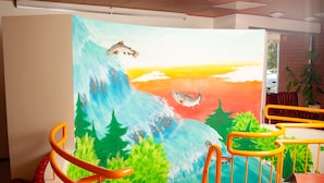 Una habitación con techo de madera, un mural colorido, una escalera con alfombra roja y una barandilla negra.