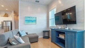 A modern living room with a grey sectional sofa, a blue entertainment unit, and a flat-screen TV mounted on the wall.