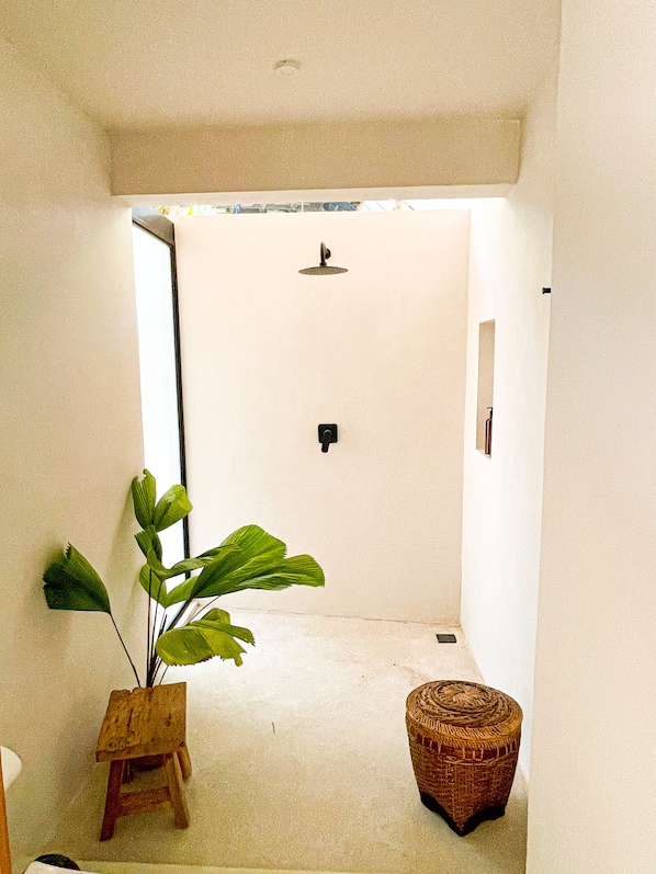 Une salle de bain avec une douche, une plante en pot et un tabouret en osier.