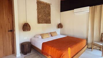 A bedroom with a wooden bed, a ceiling fan, woven wall hangings, and a small round stool.