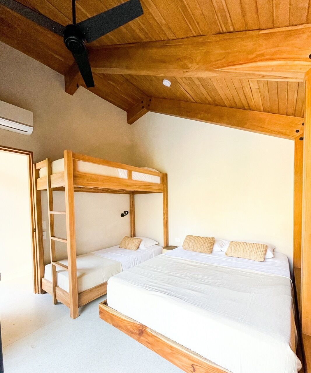 Una stanza con un letto a castello e un letto singolo, travi in legno al soffitto e una ventola a soffitto.