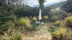 A patio with a stone floor, a green chair, a table, and an umbrella. - Villa of flowers, nestled in the green between the sea and the mountains. (Poggio dei Pini)
