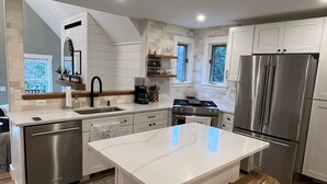 A modern kitchen with a central island, stainless steel appliances, and wooden bar stools.