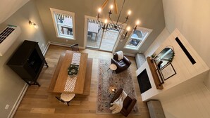 A spacious living area with a wooden dining table, two sofas, a fireplace, and large windows.