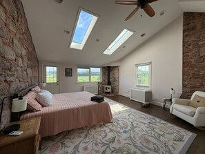 Un dormitorio con una cama grande, una zona de estar con una silla, una chimenea y tragaluces.