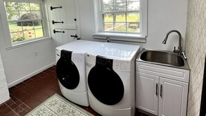 A laundry room with two washing machines, a sink, and two windows.