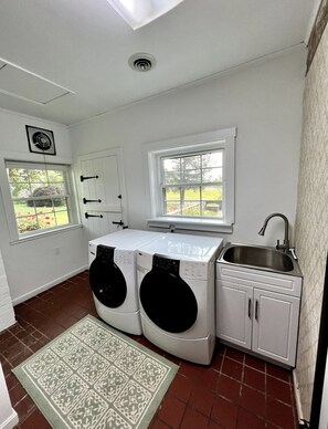 Un cuarto de lavandería con dos lavadoras, un lavabo y dos ventanas.