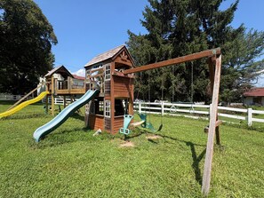 Un parque infantil con una casita de madera, toboganes y columpios.