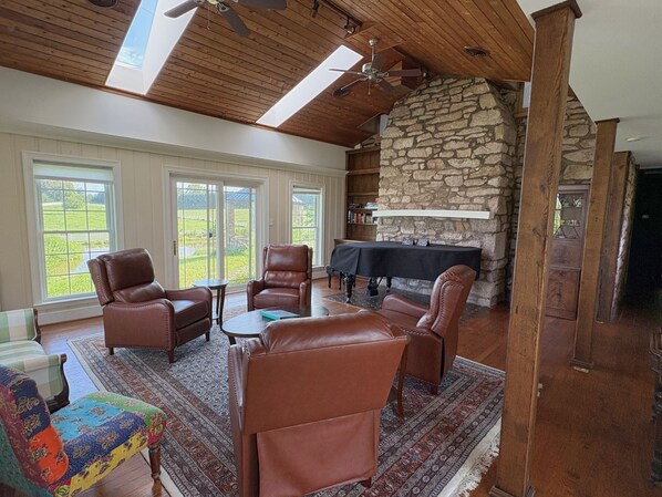 A spacious living room with leather chairs, a piano, and a stone fireplace.