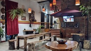 A rustic interior with wooden benches and tables, a brick wall, and hanging lights.