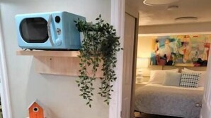 Une pièce comprenant un lit, un téléviseur fixé au mur, une plante suspendue et un meuble de rangement en osier.