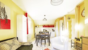 A modern living room with a sofa, dining table, and chairs. There is a kitchen area with cabinets and appliances in the background. - Comme Chez Soi - Vue montagne et garage privé (La Bresse)