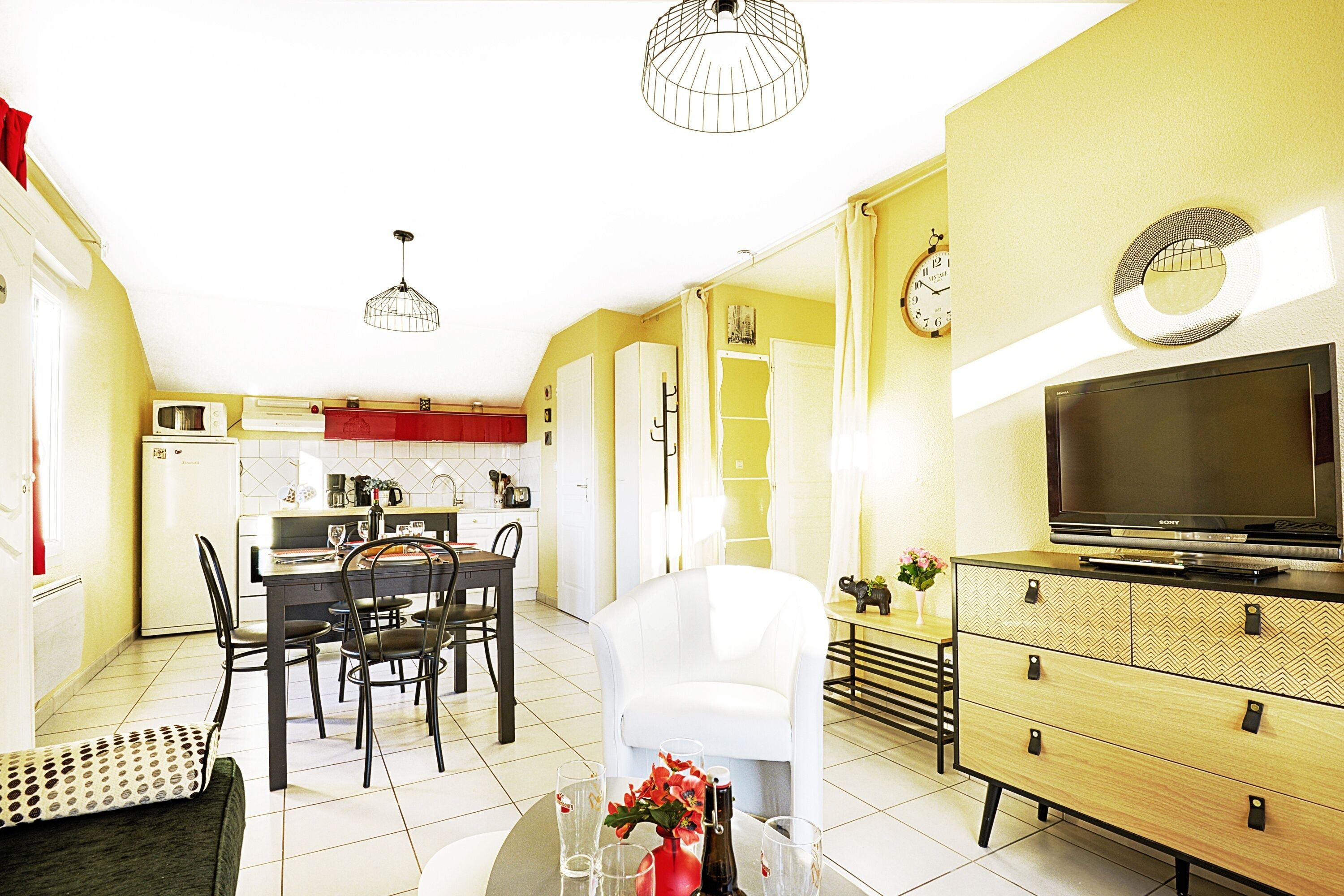 A compact living space with a dining area, kitchenette, and a TV on a wooden cabinet.