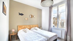 Een slaapkamer met twee bedden, een houten hoofdbord, een nachtkastje met een lamp en een raam met gordijnen.