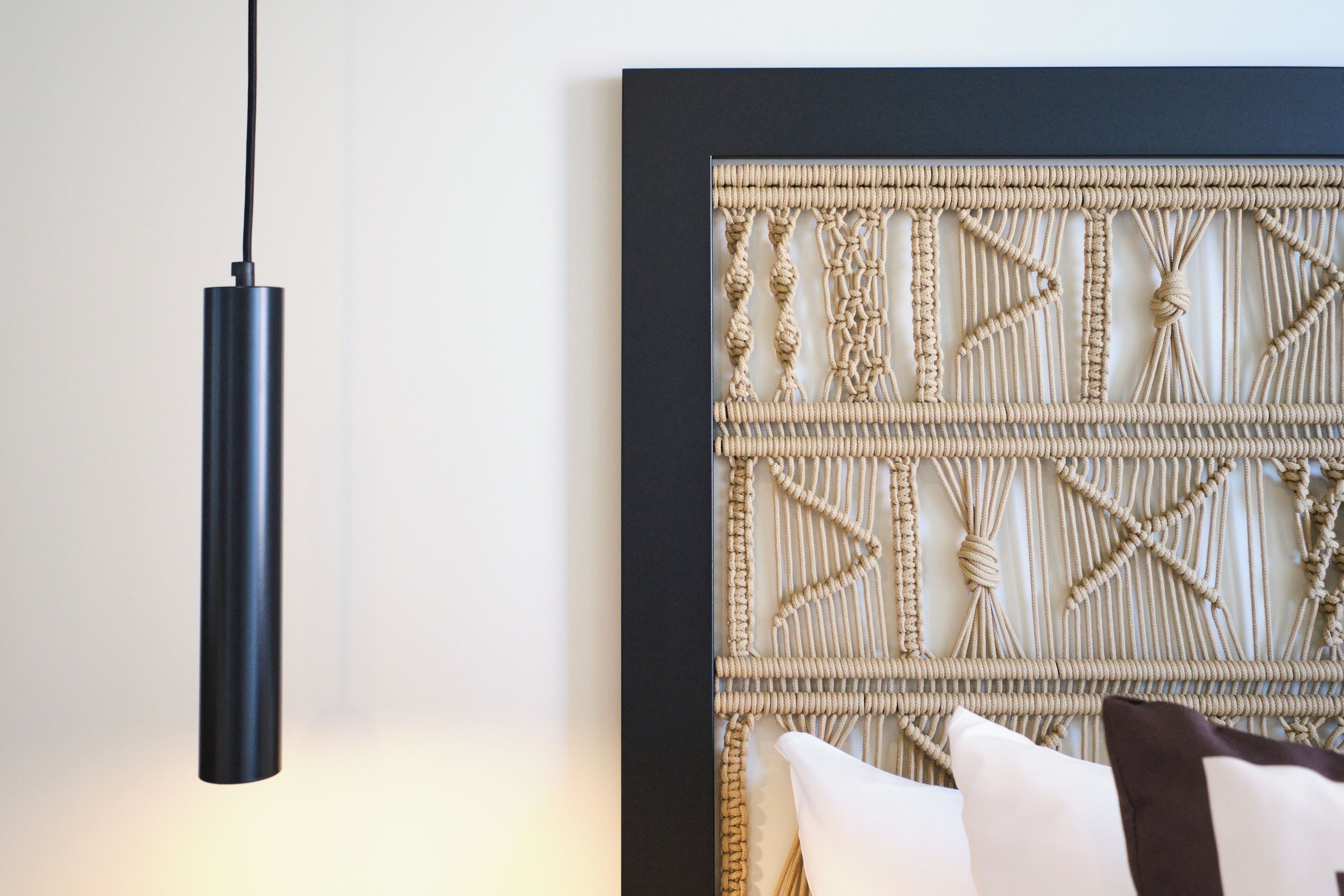 A modern room with a black pendant light, a woven wall panel, and a white pillow.