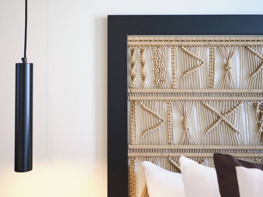 A modern room with a black pendant light, a woven wall panel, and a white pillow.