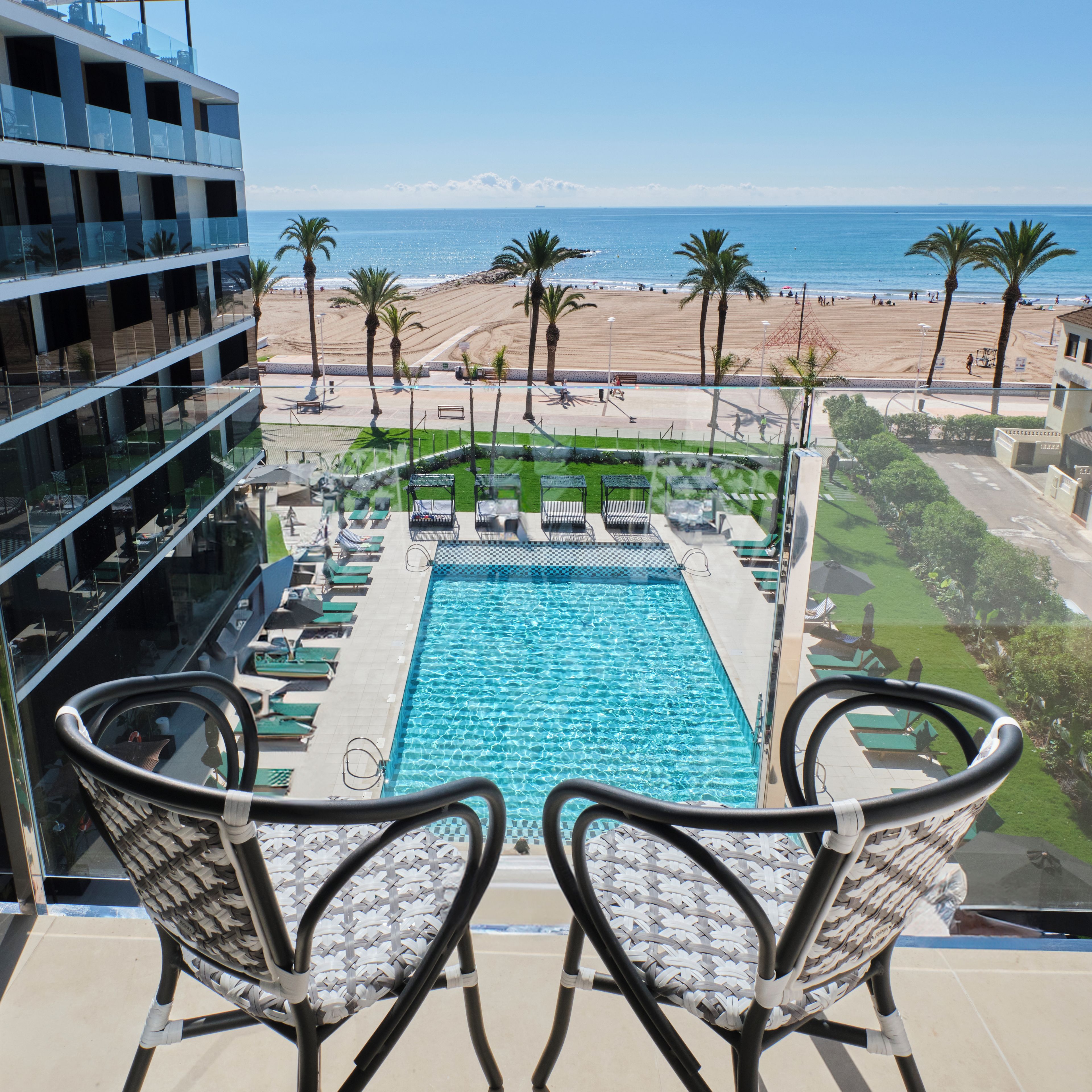 A pool with clear blue water, surrounded by lounge chairs and a view of the beach and ocean.