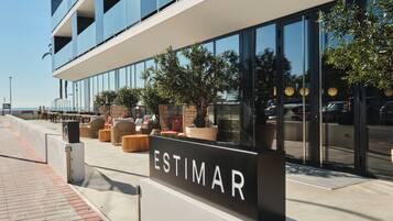 A modern building with a sign reading "ESTIMAR" and outdoor seating with potted plants.