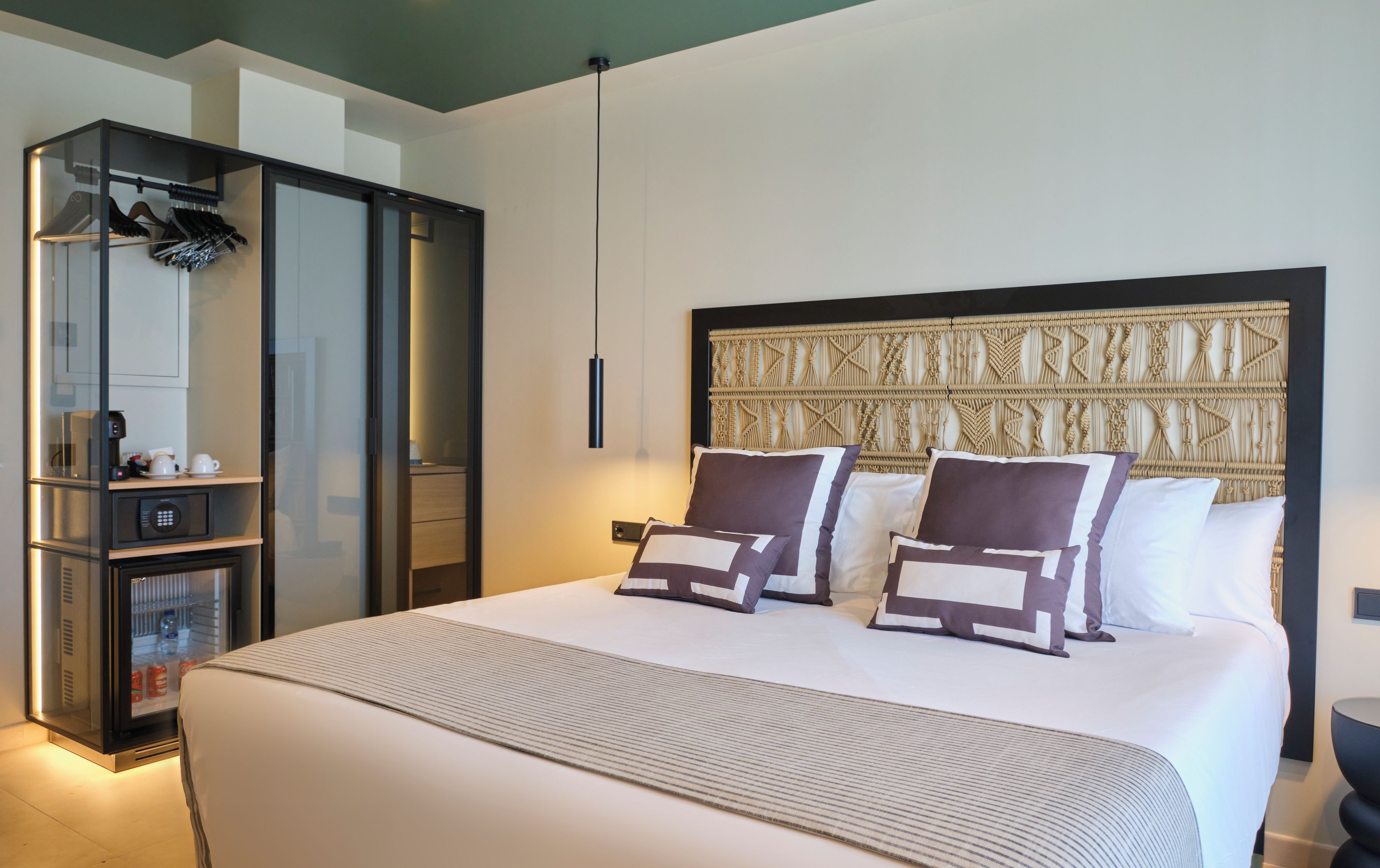 A hotel room with a large bed, a wardrobe, a minibar, and a wall-mounted headboard.