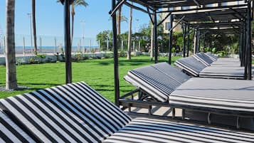 Een overdekt terras met gestreepte kussens, uitzicht op zee en palmbomen.