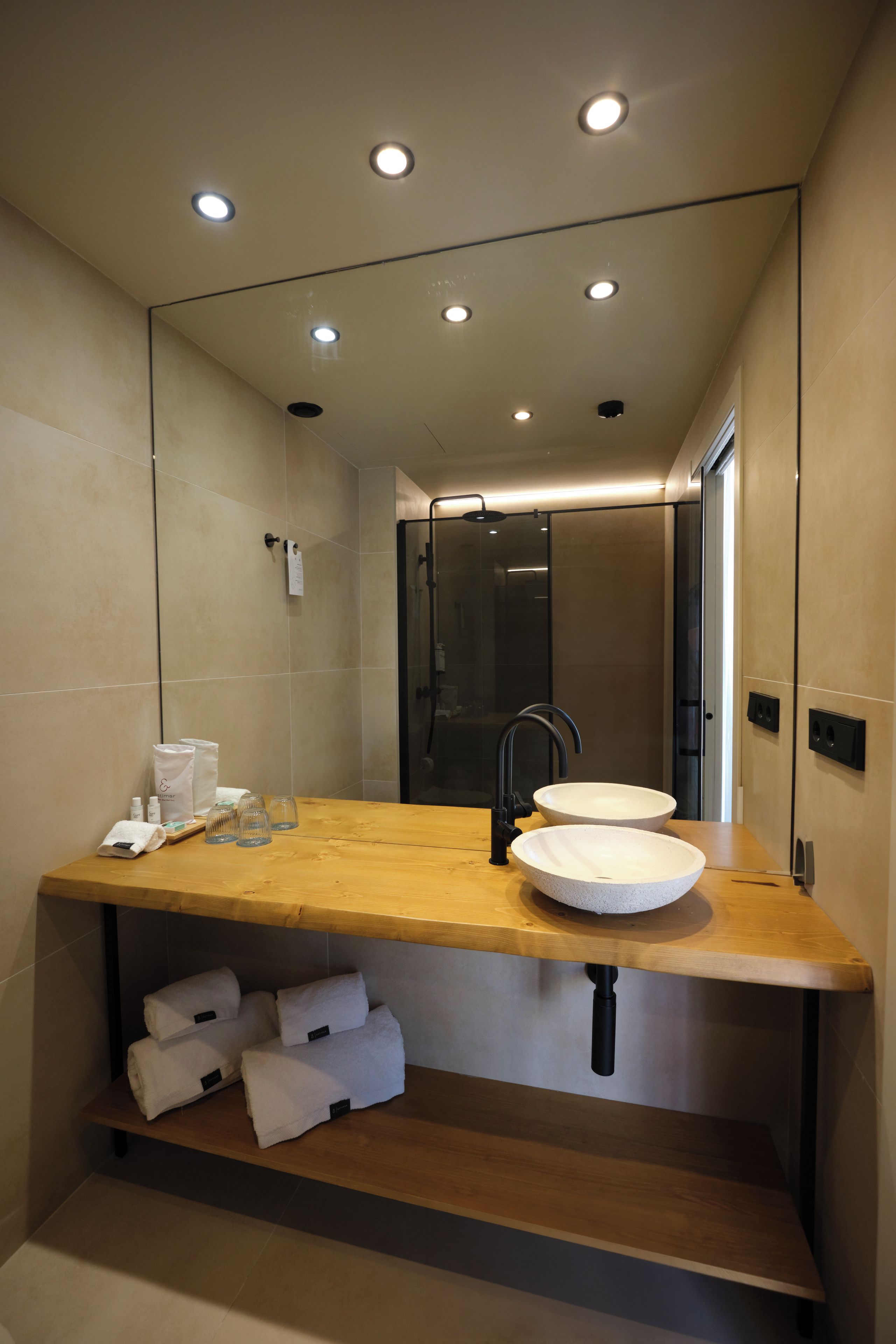 Un baño moderno con tocador de madera, dos lavamanos, un espejo y una ducha.
