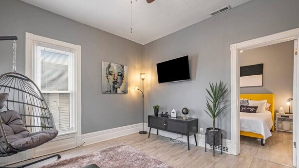 Un dormitorio moderno con cama, escritorio, silla, televisor y una planta.