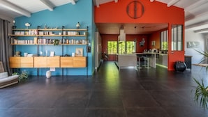 A spacious living area with a large bookshelf, a kitchen with a central island, and a bright red accent wall. - Villa Capucine, Ile de Ré (Sainte-Marie-de-Ré)