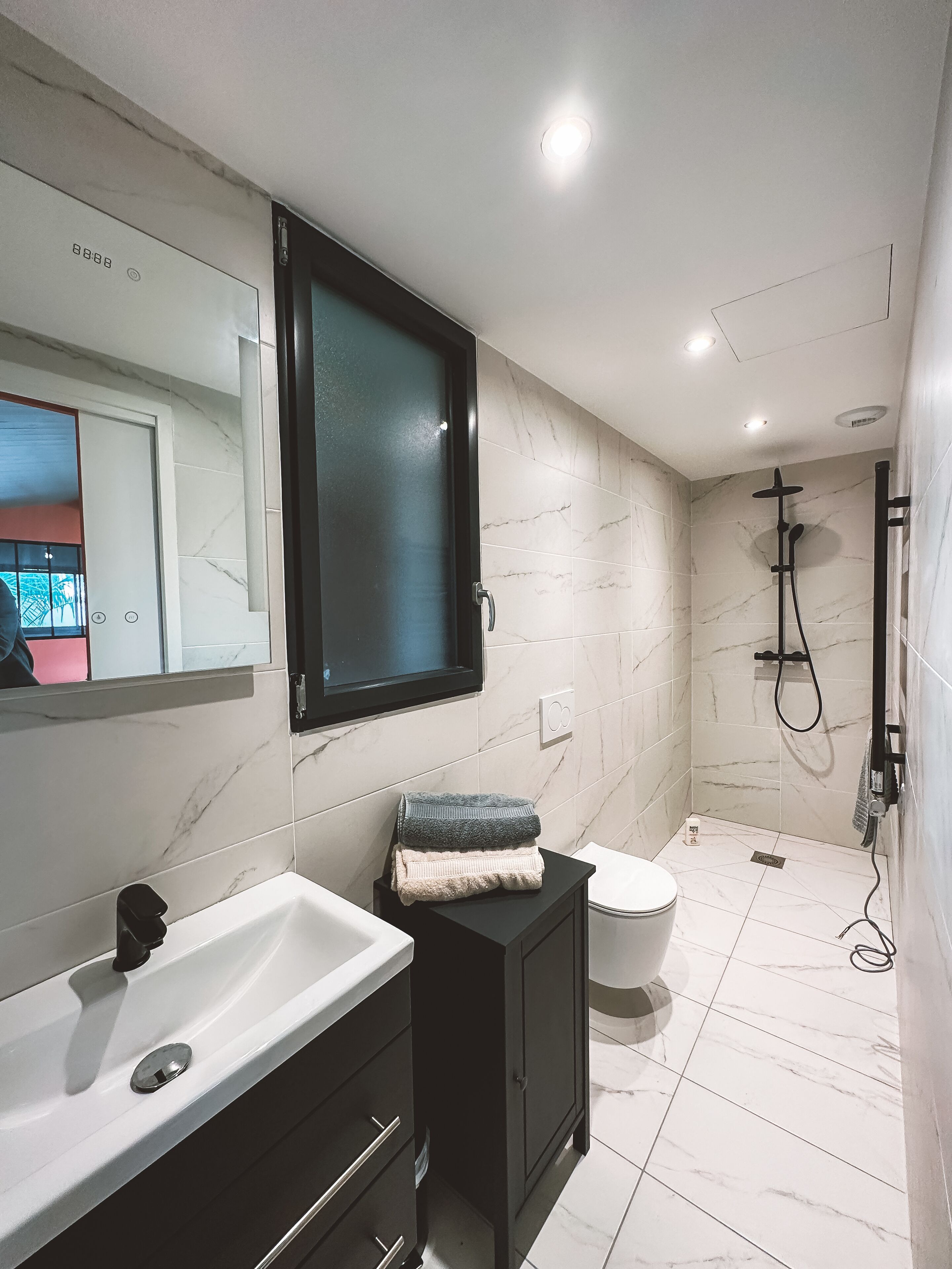 A bathroom with a white sink, dark cabinet, and a shower area with a handheld showerhead.