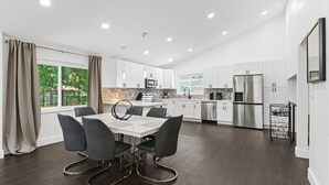 A modern kitchen with white cabinets, stainless steel appliances, and a dining area with a marble table and black chairs.