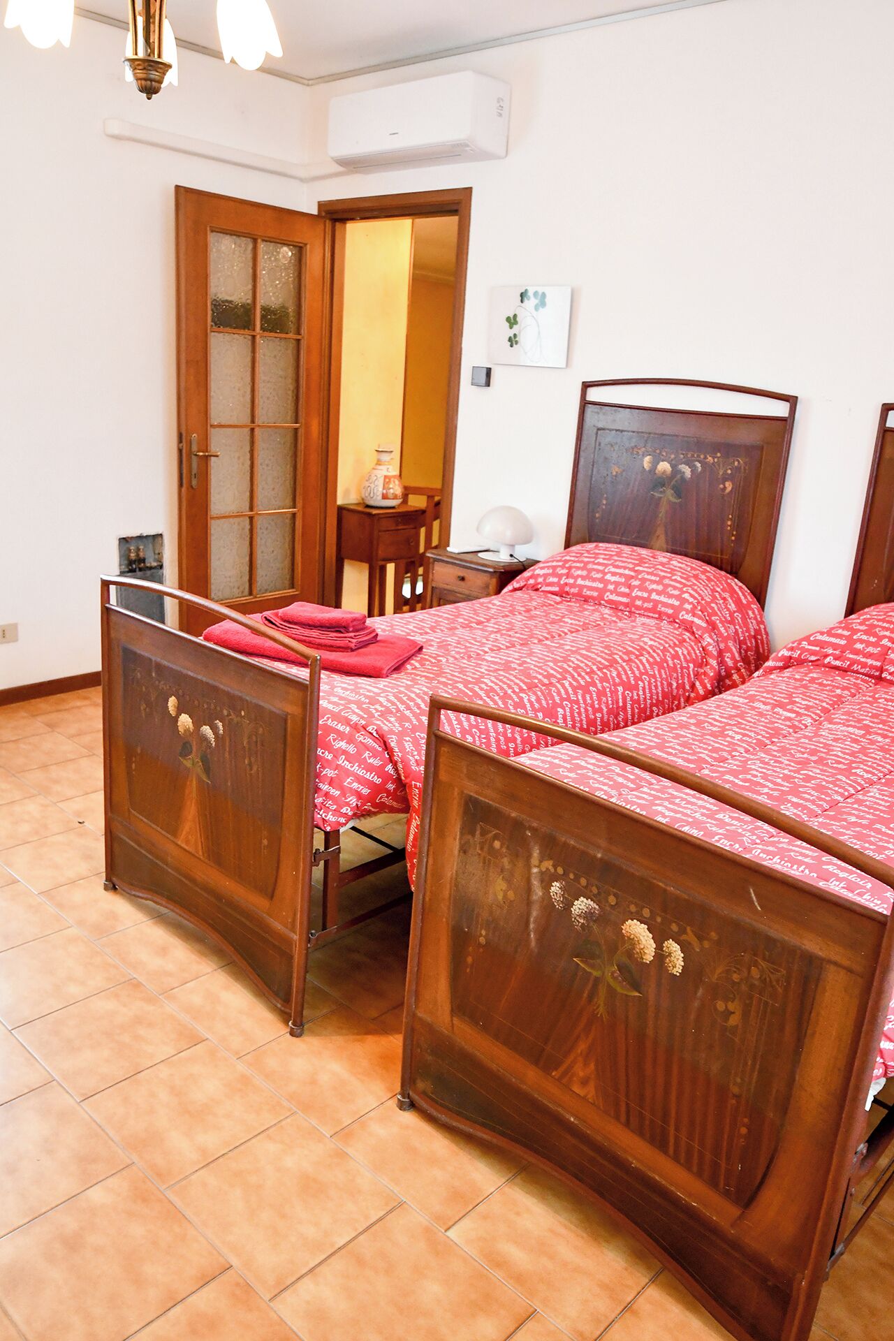 A bedroom with two wooden beds, a wooden wardrobe, a small table, and a wall-mounted air conditioner.