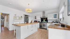 A modern kitchen with white cabinetry, a wooden island, a stainless steel range hood, and a pendant light. - Cosy 5BRLuxe House, w/Games Room, Great for Groups (Widley)