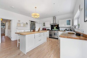 Une cuisine moderne avec des meubles blancs, un îlot central en bois, une hotte de cuisine en acier inoxydable et un luminaire suspendu.